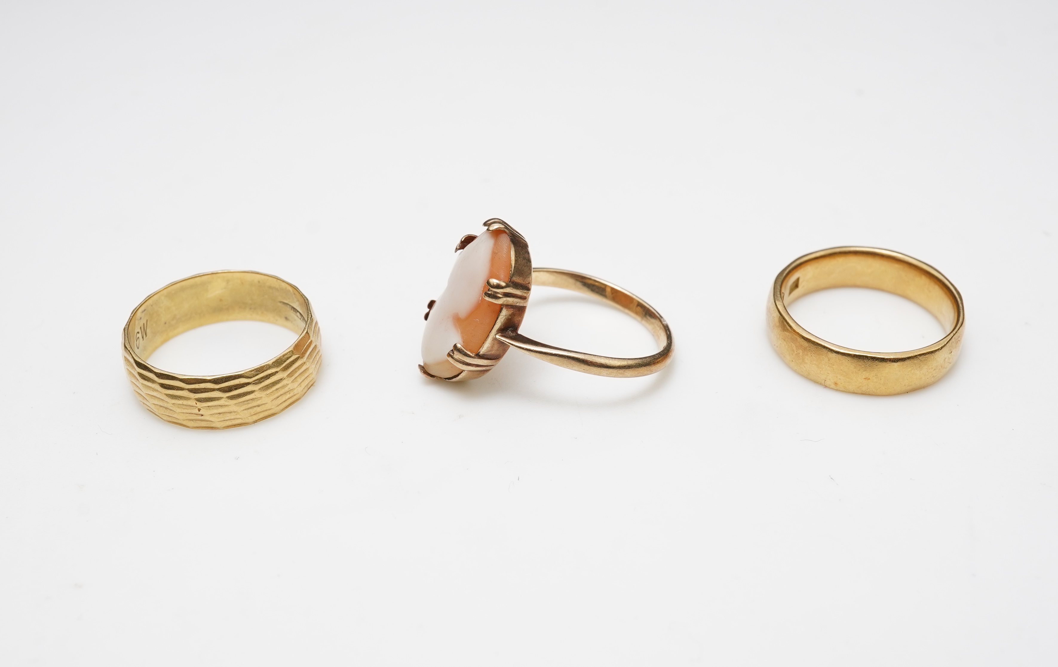 Three rings, comprising: two 18ct gold wedding bands, of planished and textured design, sizes K and L respectively, each with British hallmarks, combined gross weight approximately 11 grams; and a shell cameo ring mounte